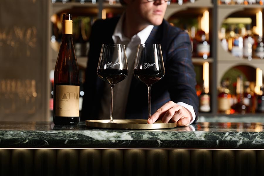 A bartender presenting two glasses of red wine at the Olivine bar